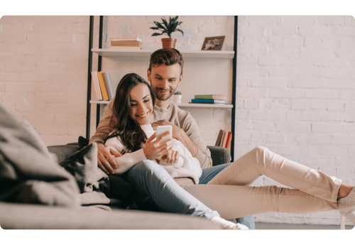 Man en vrouw zittend in een bank, lachend naar een telefoon in de hand, symbool voor het investeren in obligaties als veilige beleggingsoptie