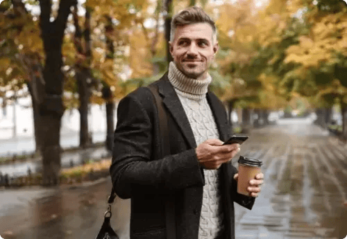 Man buiten op straat met telefoon en koffie in de hand, symbool voor de toegankelijkheid en het dagelijks volgen van beursactiviteiten