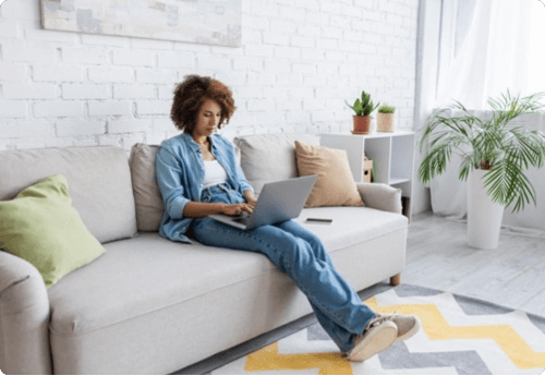 Vrouw zittend in een bank met laptop op schoot, symbool voor het verhandelen en begrijpen van derivaten in de financiële wereld.