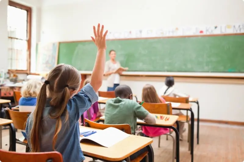Meisje op school die haar hand in de lucht steekt om een vraag te willen beantwoorden, wat symboliseert dat zij een vraag heeft over bijvoorbeeld beleggen