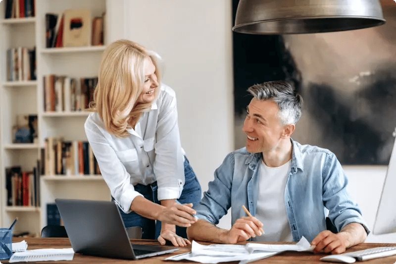 Man en vrouw kijkend naar elkaar aan tafel met papieren en laptop op tafel