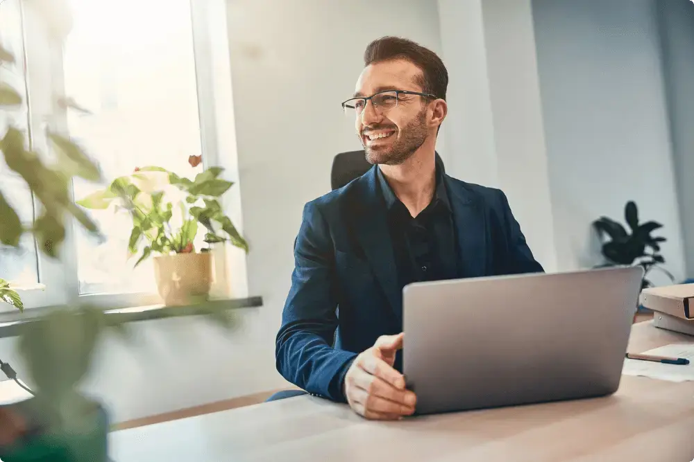 Man kijkt blij weg van zijn laptop want hij gaat voor jou beleggen