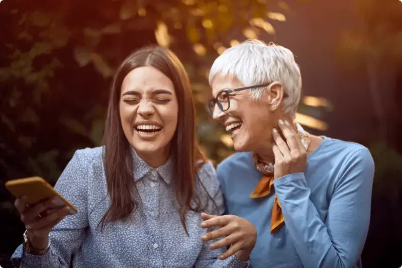 Vrouw en dochter kijken lachend naar een mobiele telefoon, nadat ze hebben uitgezocht wat beleggen inhoudt