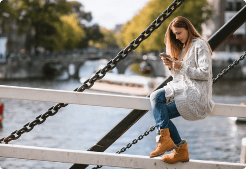 Vrouw zit op brugleuning kijkend naar telefoon om in te stappen bij Axento