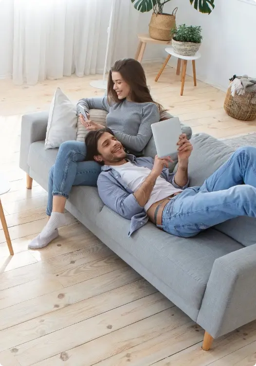 Man en vrouw liggend in de bank kijkend naar telefoon en tablet waarin axento belegt